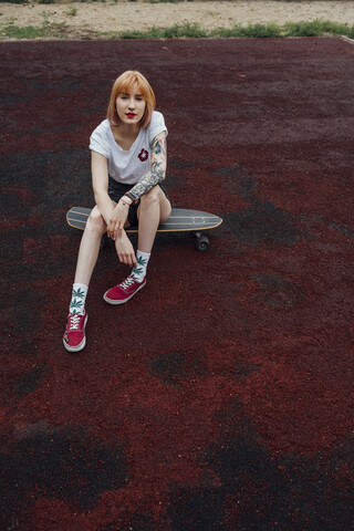 Porträt einer coolen jungen Frau, die auf einem Carver-Skateboard im Freien sitzt, lizenzfreies Stockfoto