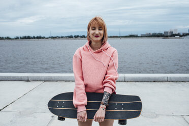 Lächelnde junge Frau mit Carver-Skateboard am Flussufer stehend - VPIF00981