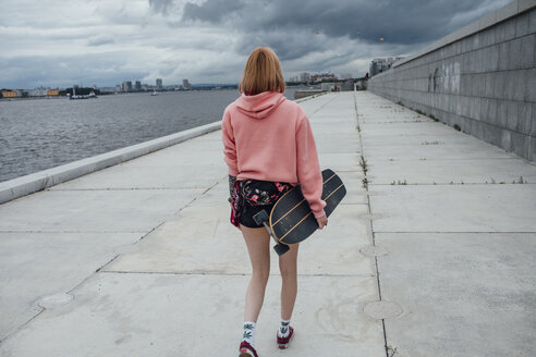 Rückansicht einer jungen Frau mit einem Carver-Skateboard am Flussufer - VPIF00983
