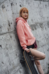 Portrait of cool young woman with carver skateboard leaning against a concrete wall - VPIF00986