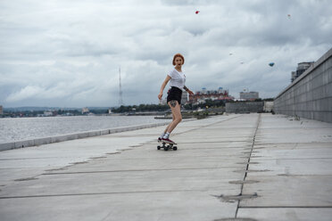 Young woman riding carver skateboard at the riverside - VPIF00988