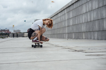 Junge Frau hockt auf einem Skateboard auf einer Promenade - VPIF00991