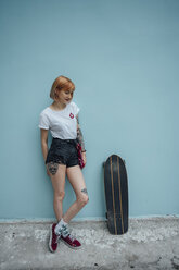 Cool young woman standing at turquoise wall next to carver skateboard - VPIF00998