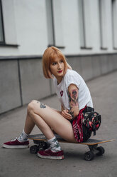 Young woman sitting on carver skateboard on the sidewalk - VPIF01004