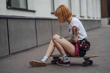 Young woman sitting on carver skateboard on the sidewalk - VPIF01006
