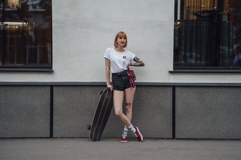 Junge Frau auf dem Bürgersteig stehend mit Carver-Skateboard, lizenzfreies Stockfoto