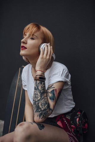 Junge Frau mit Skateboard und Kopfhörern beim Musikhören, lizenzfreies Stockfoto