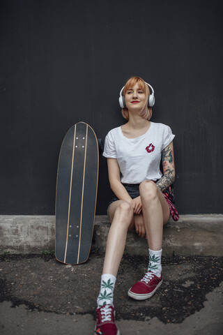Smiling young woman with skateboard and headphones sitting down listening to music stock photo