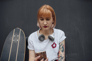 Young woman with skateboard and headphones using cell phone - VPIF01016