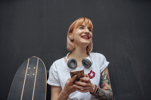 Happy young woman with skateboard, headphones and cell phone - VPIF01017