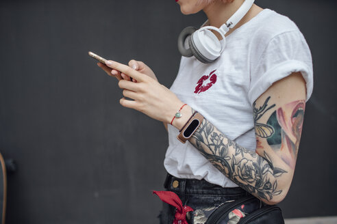 Close-up of tattooed young woman with headphones using cell phone - VPIF01021