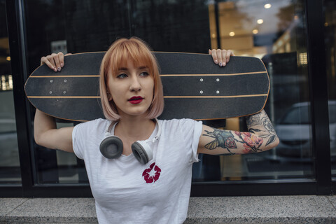 Junge Frau hält Carver Skateboard vor einem Gebäude, lizenzfreies Stockfoto