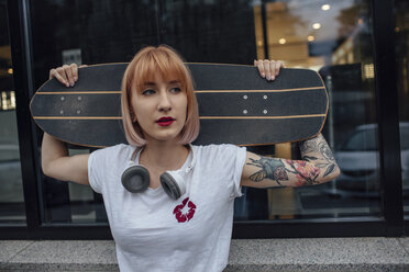 Junge Frau hält Carver Skateboard vor einem Gebäude - VPIF01022