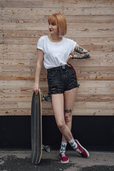 Junge Frau an Holzwand stehend mit Carver-Skateboard - VPIF01029