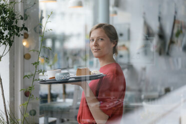 Porträt einer lächelnden jungen Frau, die Kaffee und Kuchen in einem Café serviert - KNSF05290
