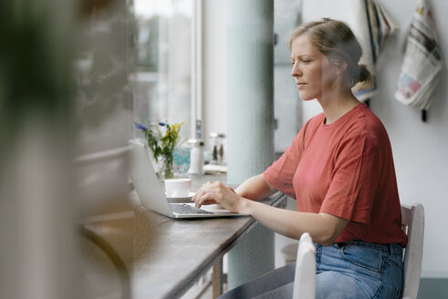 Junge Frau mit Laptop am Fenster eines Cafés - KNSF05306