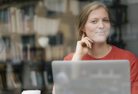 Porträt einer lächelnden jungen Frau mit Laptop in einem Café, lizenzfreies Stockfoto