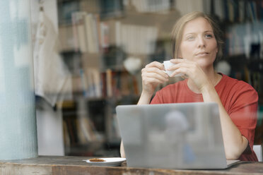 Junge Frau mit einer Tasse Kaffee und einem Laptop in einem Cafe - KNSF05308