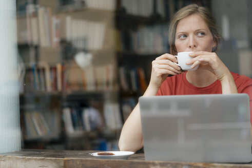 Junge Frau mit einer Tasse Kaffee und einem Laptop in einem Cafe - KNSF05309