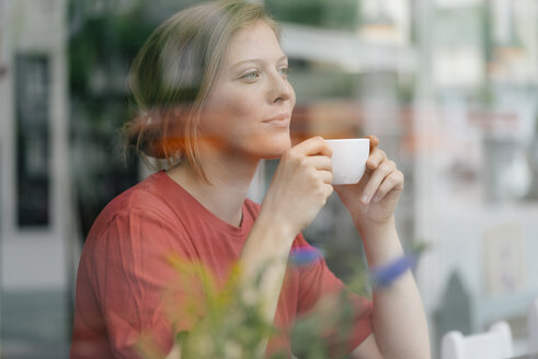 Junge Frau mit einer Tasse Kaffee hinter einer Fensterscheibe in einem Cafe - KNSF05310