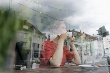 Junge Frau mit einer Tasse Kaffee hinter einer Fensterscheibe in einem Cafe - KNSF05311
