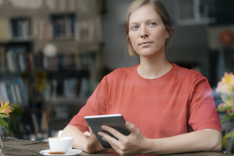 Junge Frau mit Tablet am Fenster in einem Café, lizenzfreies Stockfoto