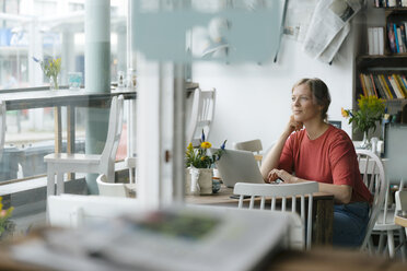 Young woman using laptop at table in a cafe - KNSF05326