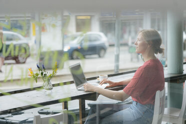 Junge Frau mit Tasse Kaffee und Laptop am Fenster eines Cafés sitzend - KNSF05328