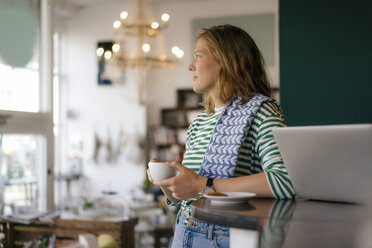 Young woman with cup of coffee and laptop in a cafe - KNSF05347