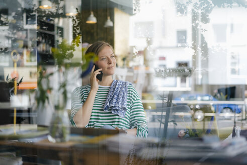 Lächelnde junge Frau am Handy in einem Café - KNSF05354