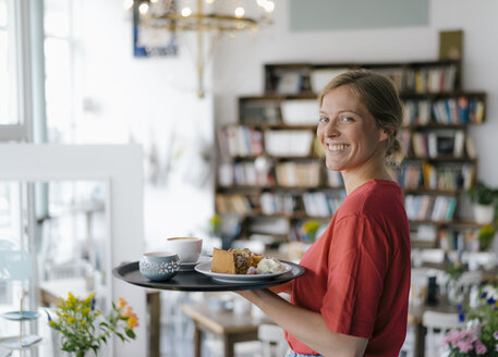 Porträt einer lächelnden jungen Frau, die Kaffee und Kuchen in einem Café serviert - KNSF05360