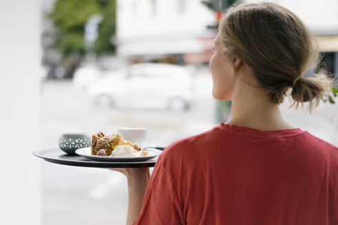 Rückansicht einer jungen Frau, die Kaffee und Kuchen in einem Cafe serviert - KNSF05362