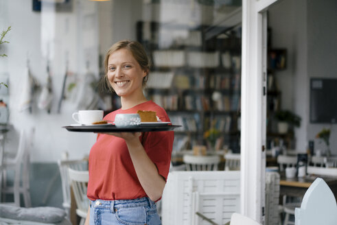 Porträt einer lächelnden jungen Frau, die Kaffee und Kuchen in einem Café serviert - KNSF05363