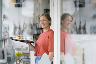 Porträt einer lächelnden jungen Frau, die Kaffee und Kuchen in einem Café serviert - KNSF05367