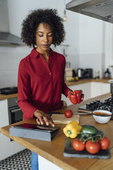 Woman standing in kitchen, chopping vegetables, using digital tablet - BOYF00961