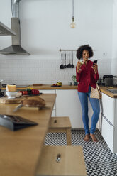 Woman drinking white wine in her kitchen, using smartphone - BOYF00973