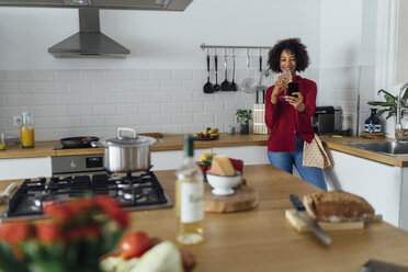 Woman standing in her kitchen, taking a selfie, drinking wine - BOYF00976