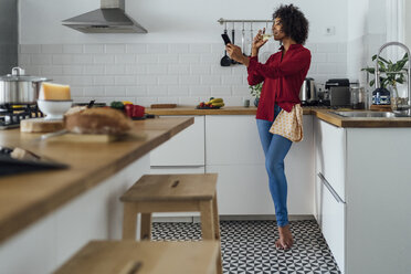 Woman standing in her kitchen, taking a selfie, drinking wine - BOYF00977