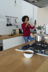 Frau trinkt Weißwein in ihrer Küche und benutzt ihr Smartphone - BOYF00978
