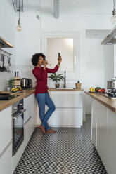 Woman standing in her kitchen, taking a selfie, drinking wine - BOYF00979