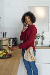 Woman standing in her kitchen, with a glass of wine, using smartphone - BOYF00981