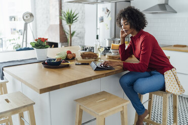 Woman sitting in kitchen with a glass of white wine, using digital tablet - BOYF00989