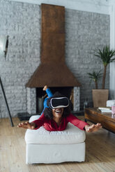 Woman lying on seating furniture, wearing VR goggles, pretending to fly - BOYF01003