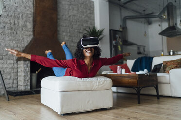 Woman lying on seating furniture, wearing VR goggles, pretending to fly - BOYF01004