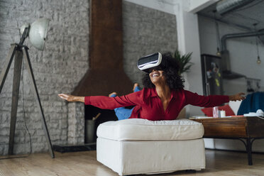 Woman lying on seating furniture, wearing VR goggles, pretending to fly - BOYF01005