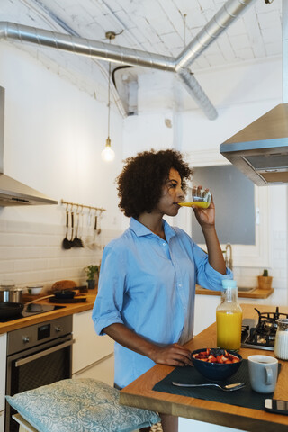 Frau frühstückt in ihrer Küche und trinkt Orangensaft, lizenzfreies Stockfoto