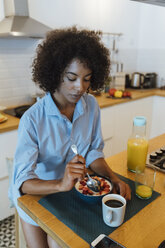 Frau frühstückt in ihrer Küche und isst Obst - BOYF01010