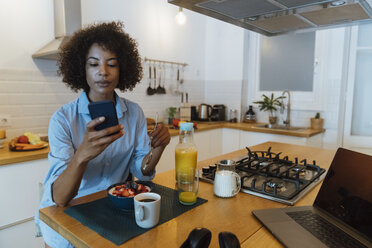 Woman having breakfast in her kitchen, using smartphone - BOYF01011