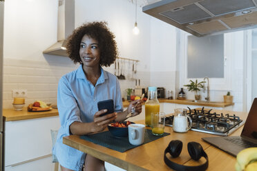 Frau frühstückt in ihrer Küche und benutzt ihr Smartphone - BOYF01012