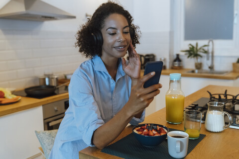 Frau mit Kopfhörern, die in ihrer Küche ein Smartphone benutzt, lizenzfreies Stockfoto